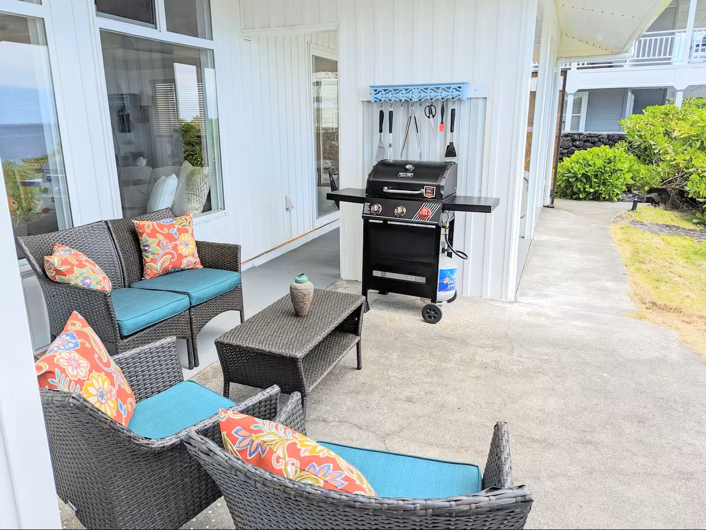Covered lanai with wicker seating, colorful tropical cushions, and gas BBQ grill