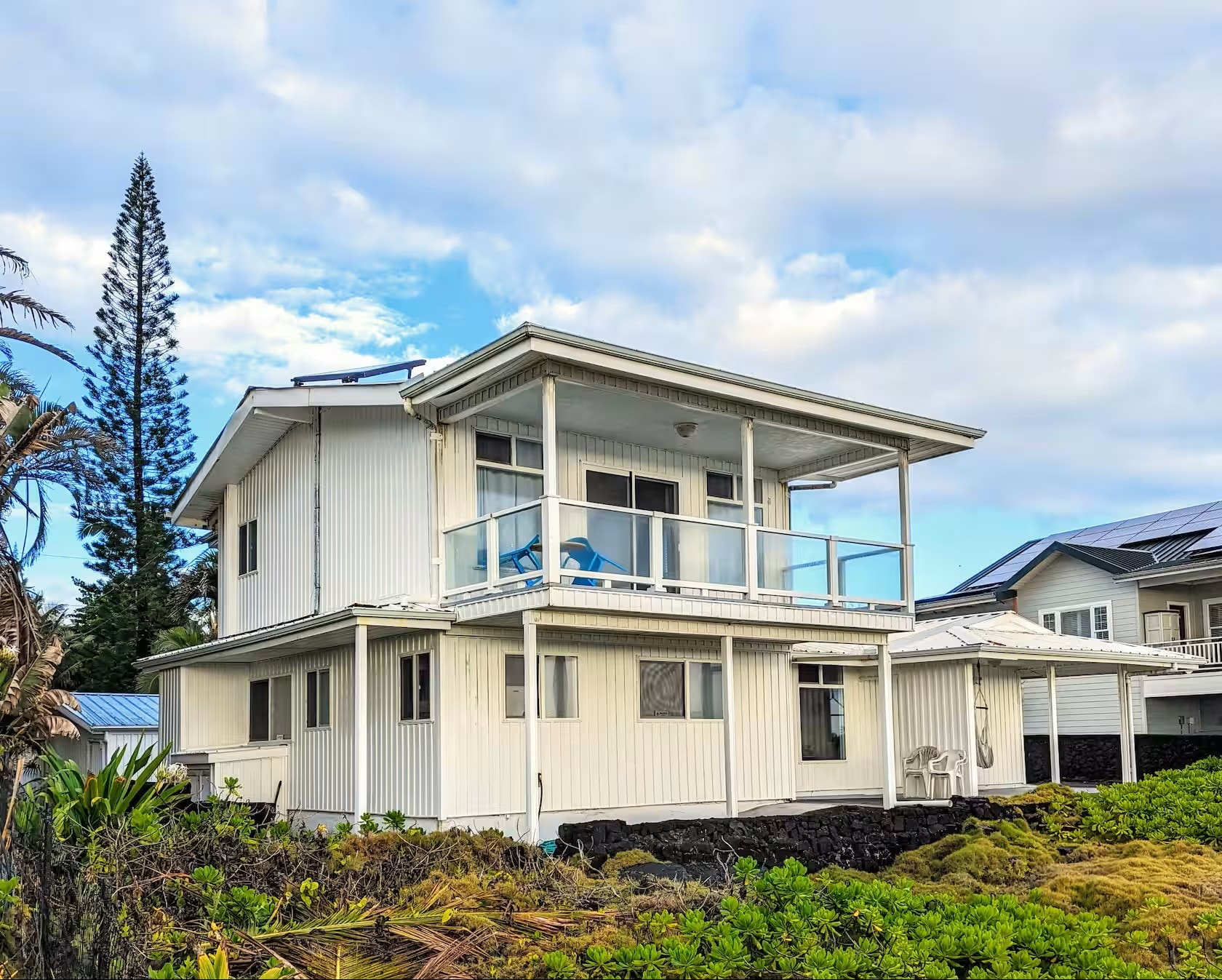 Rear view of Maka Ala Lani showing two-story white house with glass railing balcony and lava rock foundation