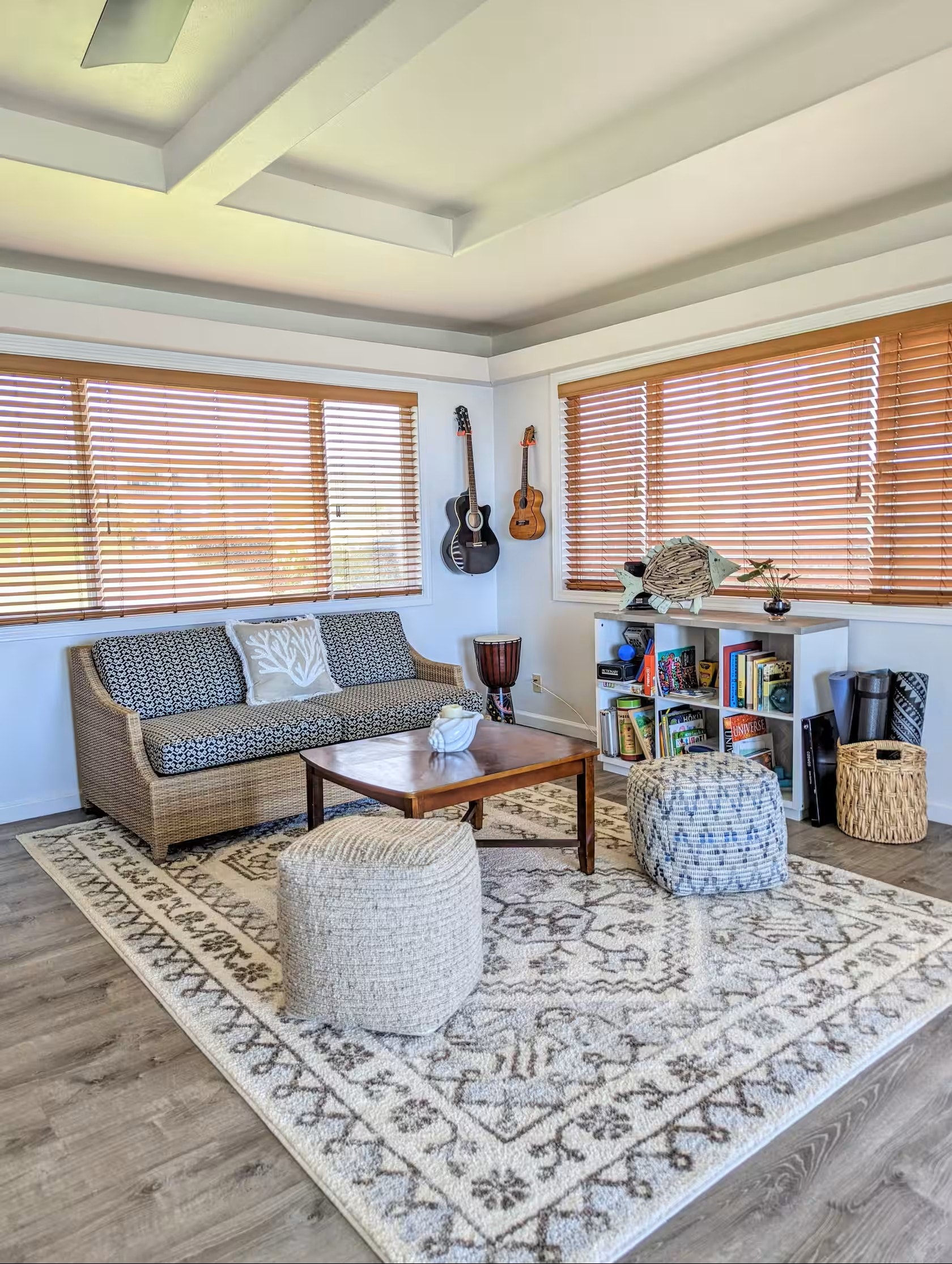 Bright reading room with wicker sofa, guitars on the wall, bookshelf, and warm bamboo blinds